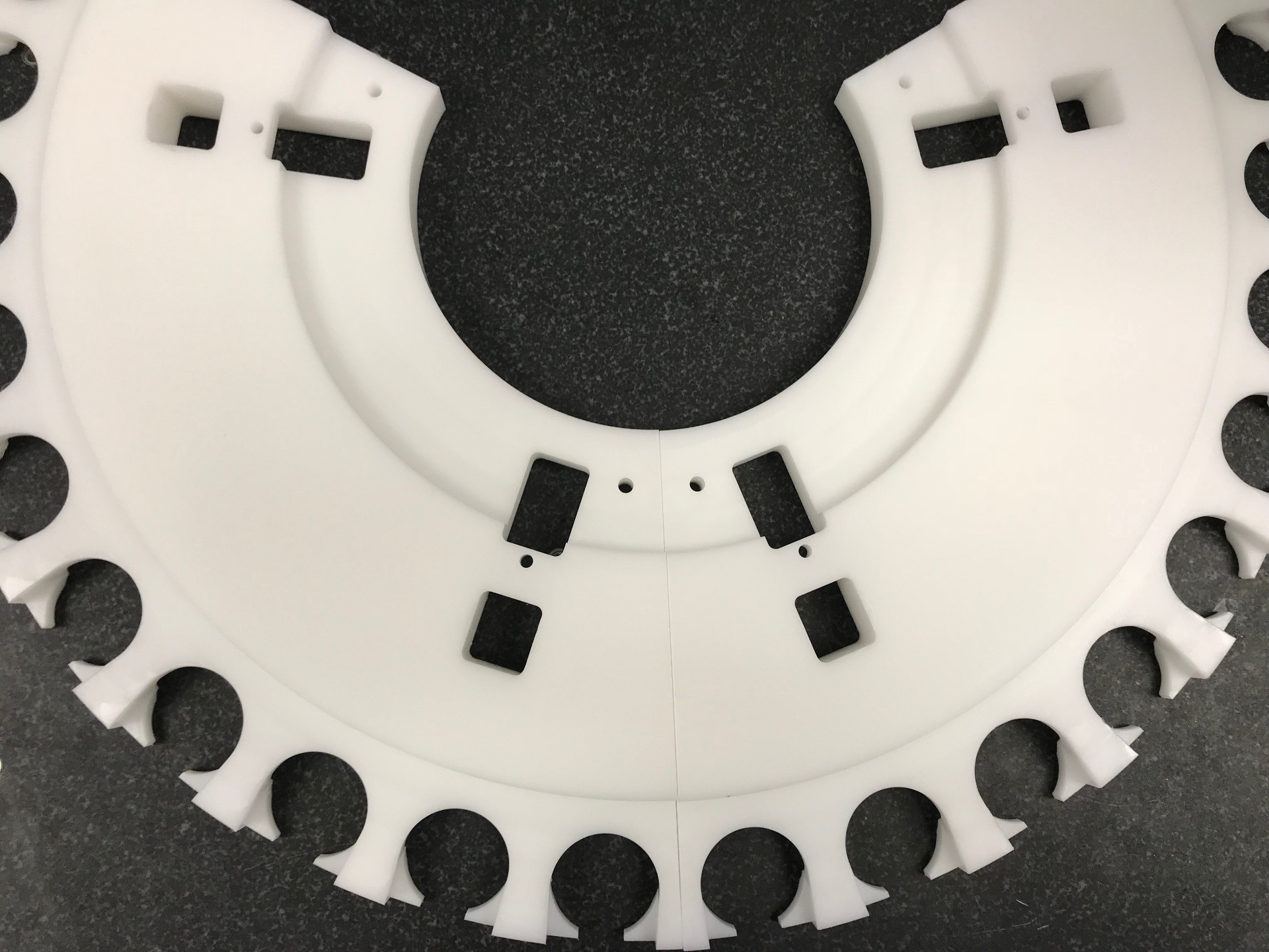 Two large white machined plastic ring segments with cutouts and slots