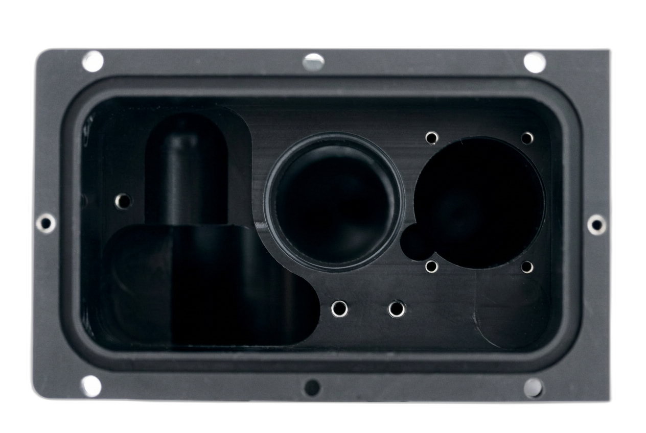 Black machined plastic rectangular housing with deep internal pocket, large bores and threaded mounting holes